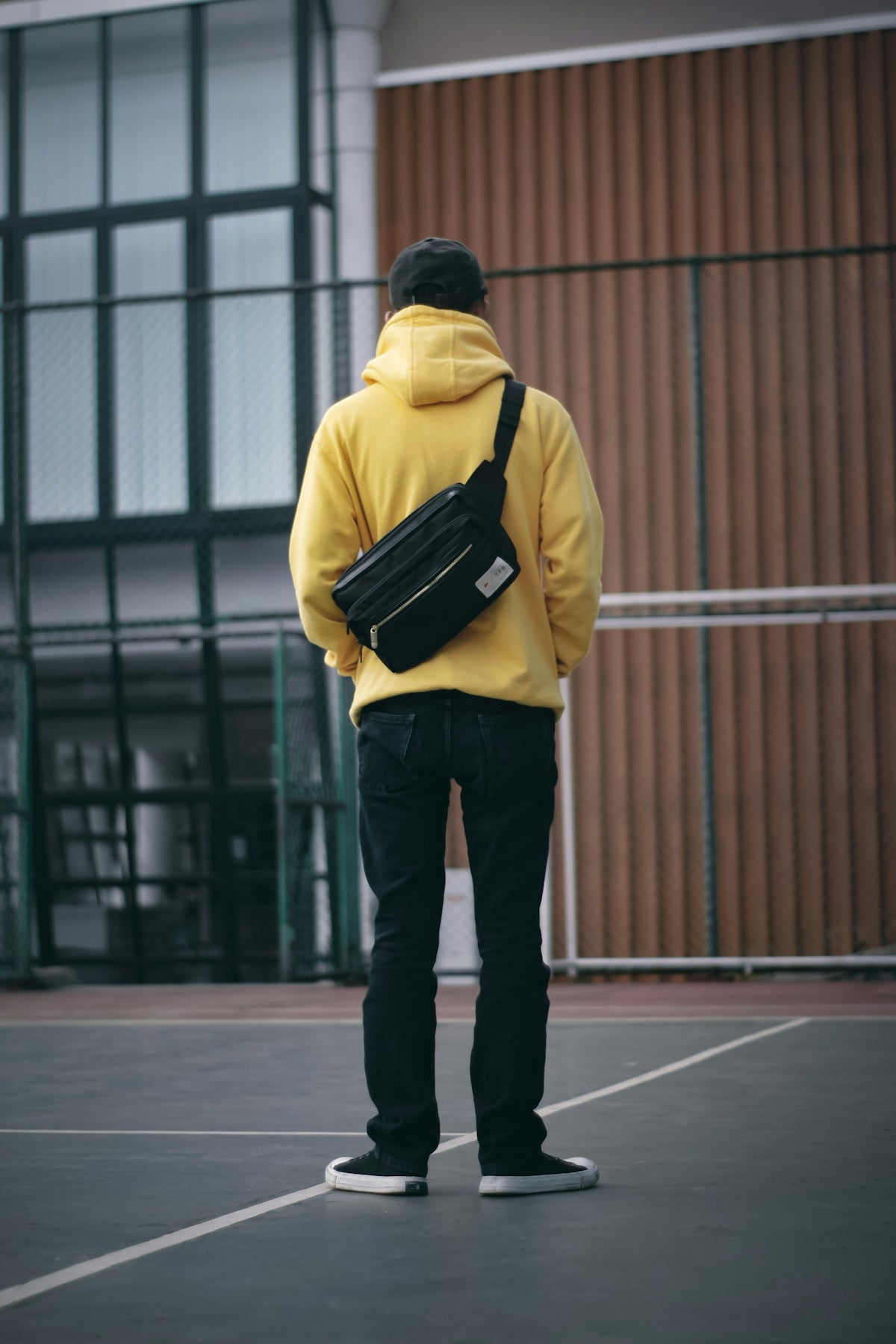 Man in yellow hoodie with crossbody bag stands on court