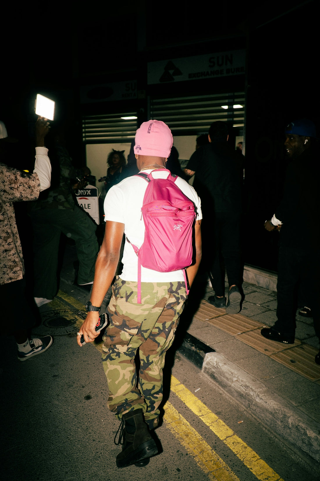 Man in pink hat and camouflage pants walks at night.